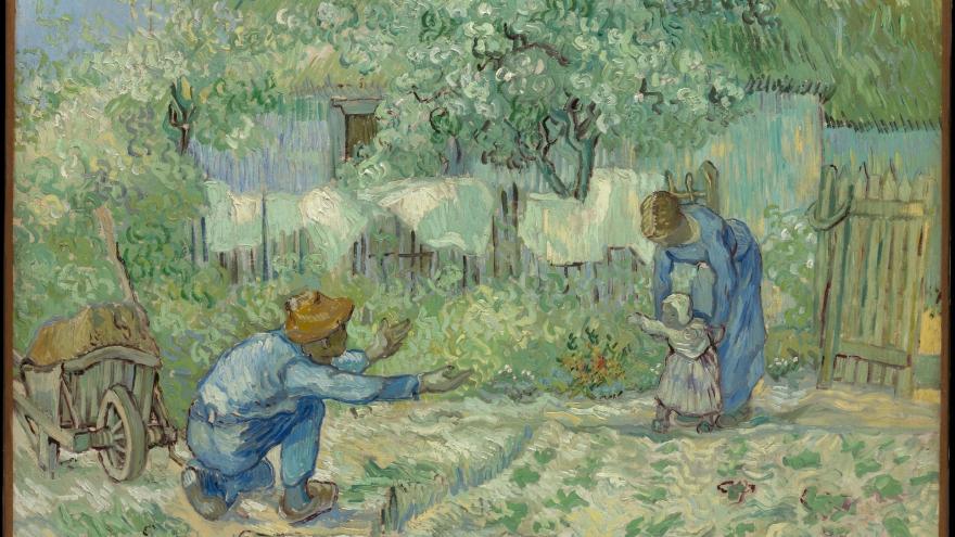 Man crouching, encourAging a child to walk, with a woman holding the child in a garden setting