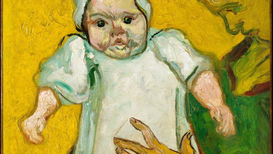 Woman holding a baby dressed in white against a yellow background