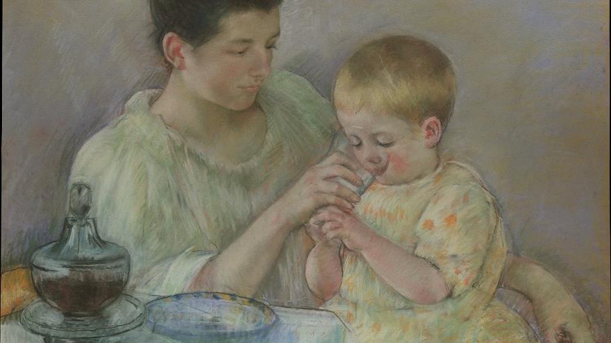 Woman helping a child drink from a glass at a table