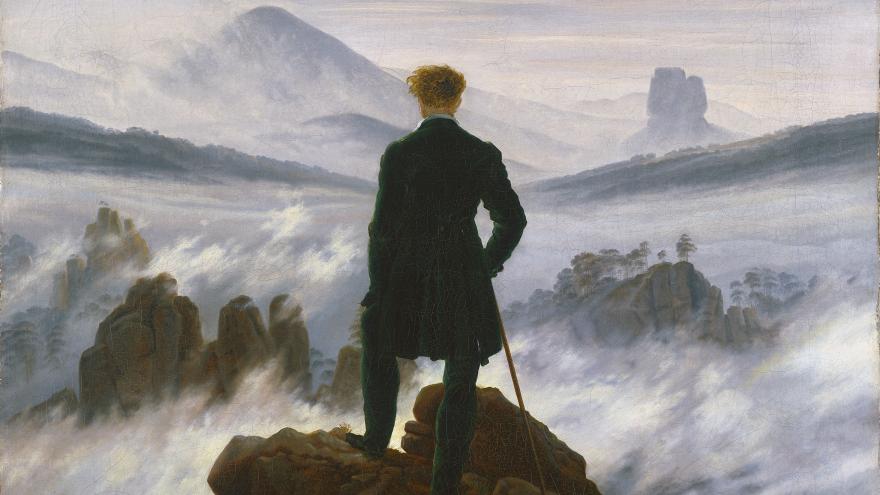 Figure standing on cliff overlooking foggy landscape